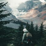 anmol A traveler in a green jacket hikes through lush forests with towering mountains in the background.