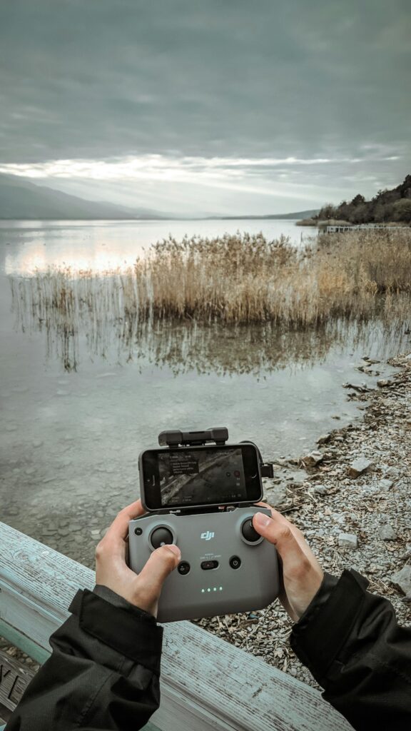 Hands operating a drone controller with a scenic lake view in the background.
