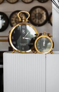 Elegant gold plated analogue clocks with Roman numerals in a vintage shop setting.