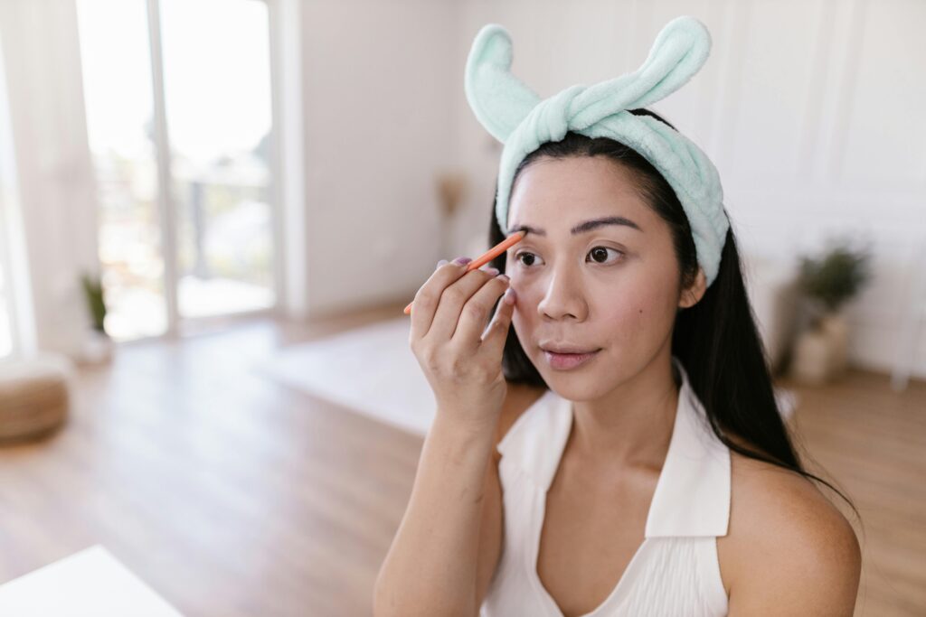 Woman using an eyebrow pencil indoors, focusing on personal makeup routine.