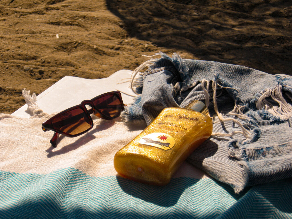 Sunglasses and sunscreen on a towel by the beach, capturing the essence of summer relaxation.