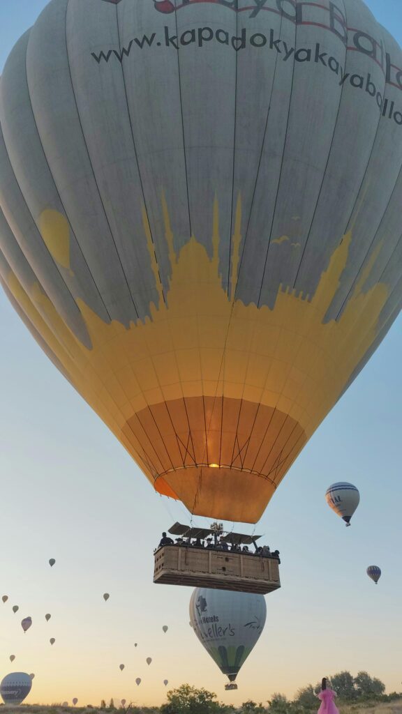 Colorful hot air balloons lift into the early sky over the scenic Cappadocia landscape.