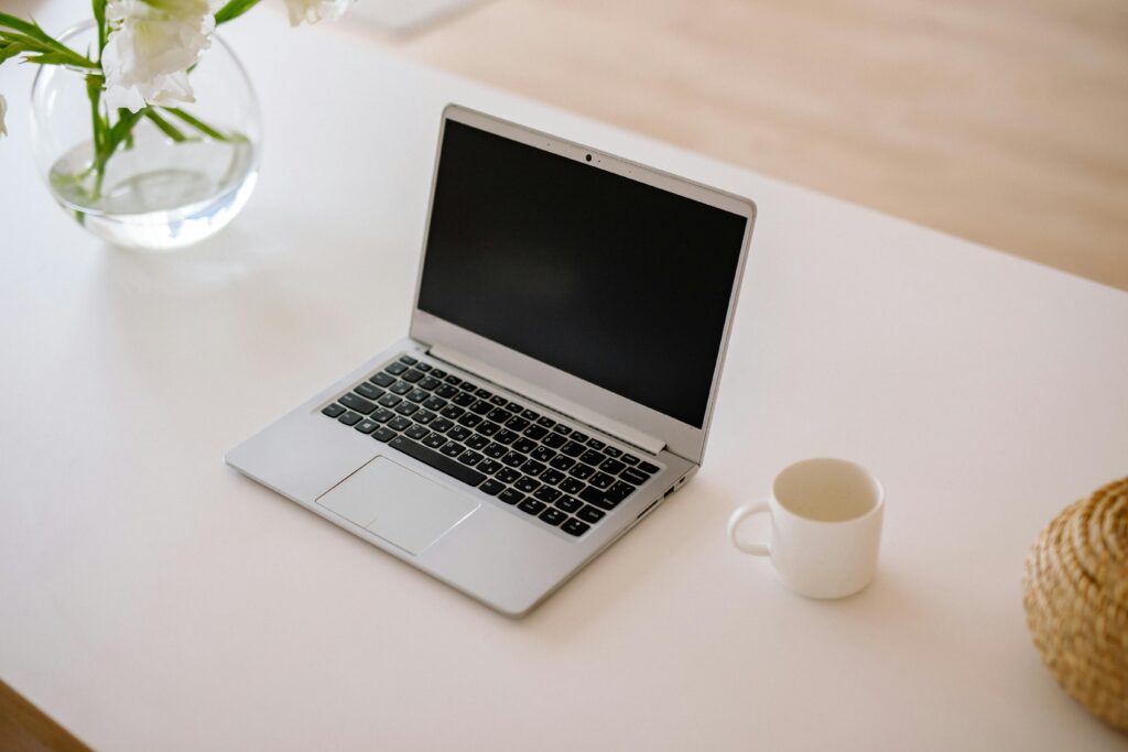 Laptop A minimalist workspace with an open laptop, coffee mug, and vase on a bright indoor table.