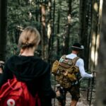 anmol A couple hikes with backpacks and poles, exploring a dense forest on a sunny day.